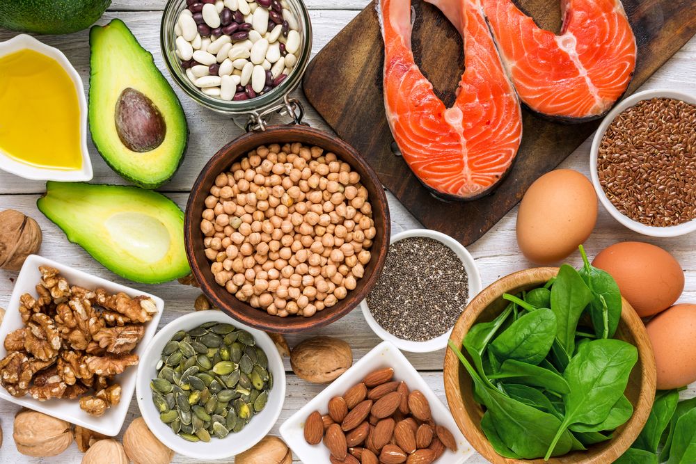 Photo of Avocado, fish, eggs, assorted nuts, and other healty foods placed in a wooden table